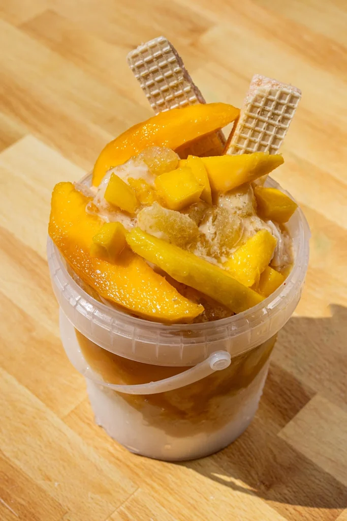 Mango bucket raspado topped with fresh mango slices, diced mango, ice cream, and wafer cookies from SoCal Frozen MX.
