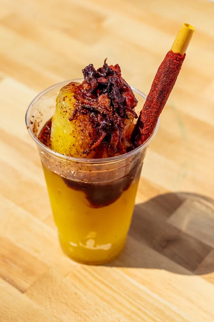 Pineapple Diablo raspado topped with chamoy, chili seasoning, and a tamarind candy stick.